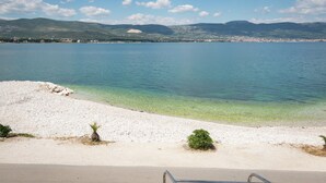 Vista costeira com praia deserta, águas calmas e montanhas ao longe.