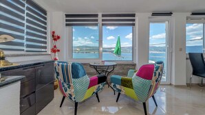 Cozinha moderna com vista para o mar, duas cadeiras coloridas e um guarda-sol verde.