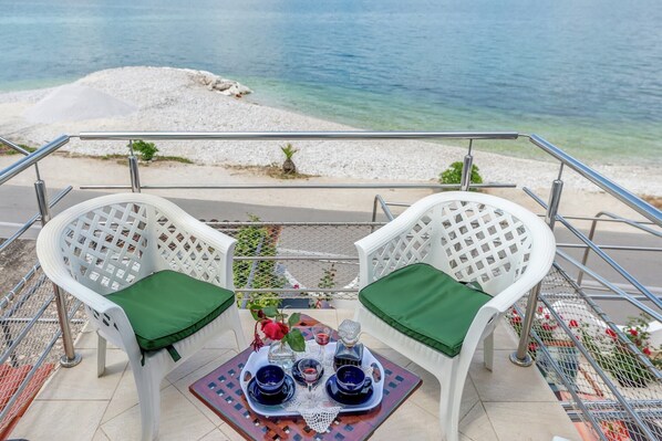A terrace with two white chairs, green cushions, and a tray with blue cups and a glass.