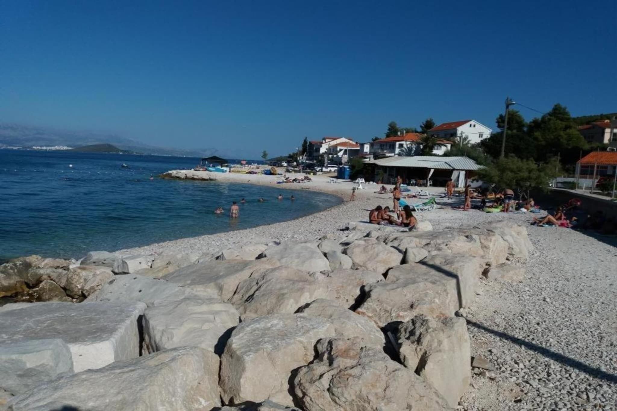 A beach with large rocks in the foreground, a sandy shore, and buildings in the background.