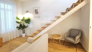 Una sala de estar moderna con una escalera, una planta en maceta, una mesa redonda de madera y un sillón gris.