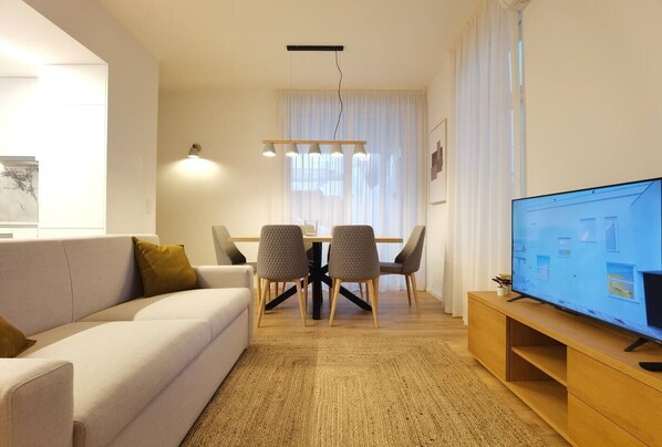 A modern living room with a sofa, dining table, chairs, and a television.