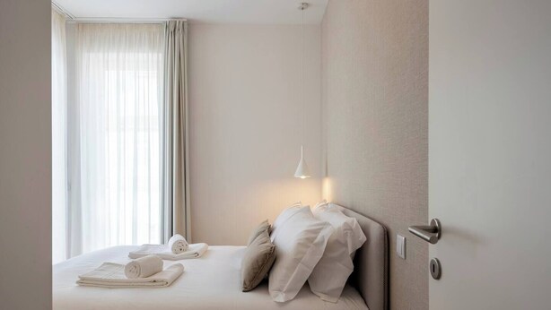 Una habitación de hotel con una cama, una mesita de noche con control remoto y una ventana con cortinas.
