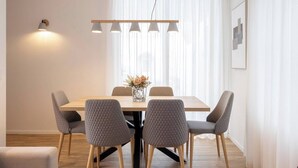 Un comedor con una mesa de madera, cuatro sillas tapizadas en gris, un florero con flores y lámparas colgantes arriba.