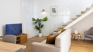 Una sala de estar moderna con un televisor de pantalla plana, una planta en maceta, una escalera y un sillón gris.