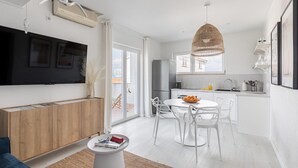 Uma cozinha moderna com armários brancos, uma área de jantar com mesa e cadeiras redondas, e uma janela grande que oferece luz natural.
