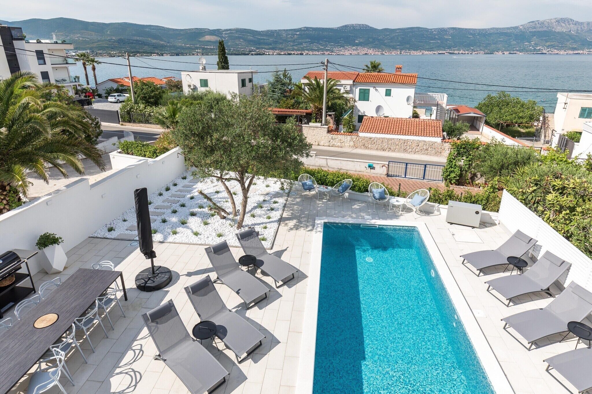 Ein Pool auf dem Dach mit Liegestühlen und Grillplatz, mit Blick auf eine Küstenstadt mit Gebäuden und Meerblick.