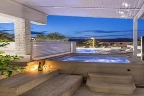A hot tub with steps and a seating area, surrounded by a covered patio with a view of a swimming pool and buildings in the background. - Modern Apartment with pool and terrace (Slatine)