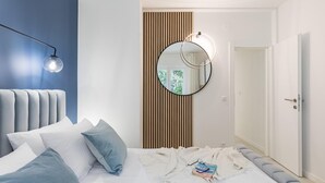 Une chambre à coucher moderne avec une tête de lit capitonnée, un miroir rond, une lampe de chevet et un lit bien fait, agrémenté d’oreillers et d’une couverture.