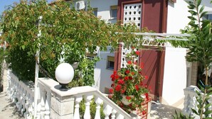 A two-story building with a red and white facade, a balcony with a white balustrade, and a potted red flower plant. - Apartment in Vinisce 100m from the Sea (Vinisce)
