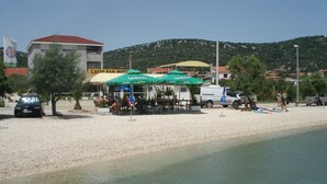 A beachside café with outdoor seating and umbrellas, a white van, and a building with a sign in the background. - Apartment in Vinisce 100m from the Sea (Vinisce)