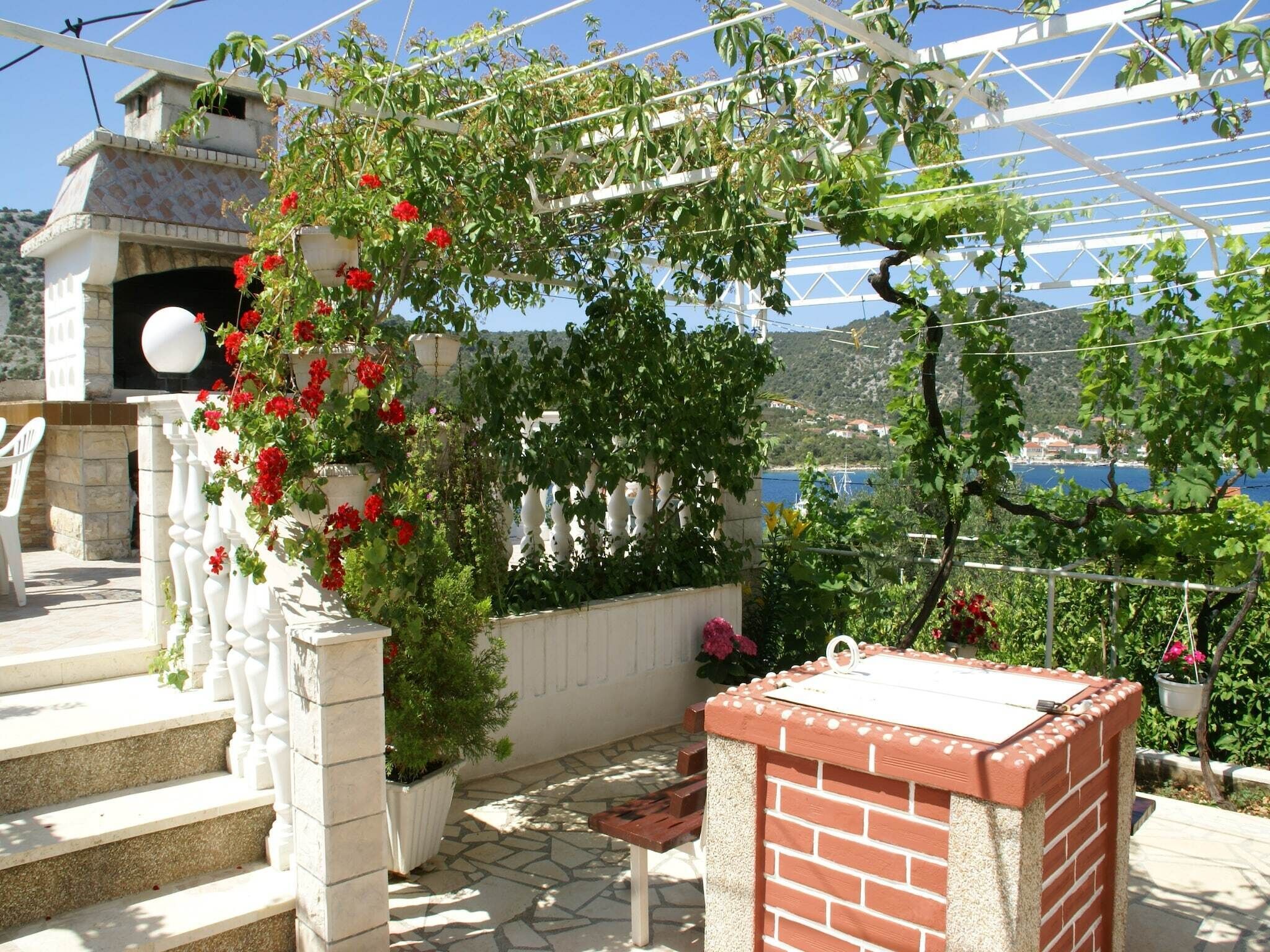 Ein Dachgarten mit Grillplatz aus Ziegeln, einem weißen Geländer und Blick aufs Meer.