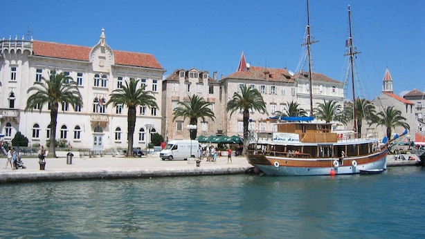 A waterfront scene with a historic building, palm trees, and a traditional wooden boat docked at the pier. - Apartment in Vinisce 100m from the Sea (Vinisce)