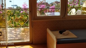 A room with a bed, a window with a view of a body of water and boats, and a balcony with flowers. - Apartment in Vinisce 100m from the Sea (Vinisce)