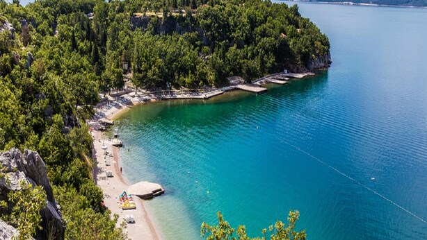 Et kystområde med strand, klart blåt vand og en halvø med skov.