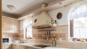 A kitchen with wooden cabinets, a microwave, a sink, and a window with lace curtains. - Spacious Holiday Home in Verteneglio (Brtonigla)