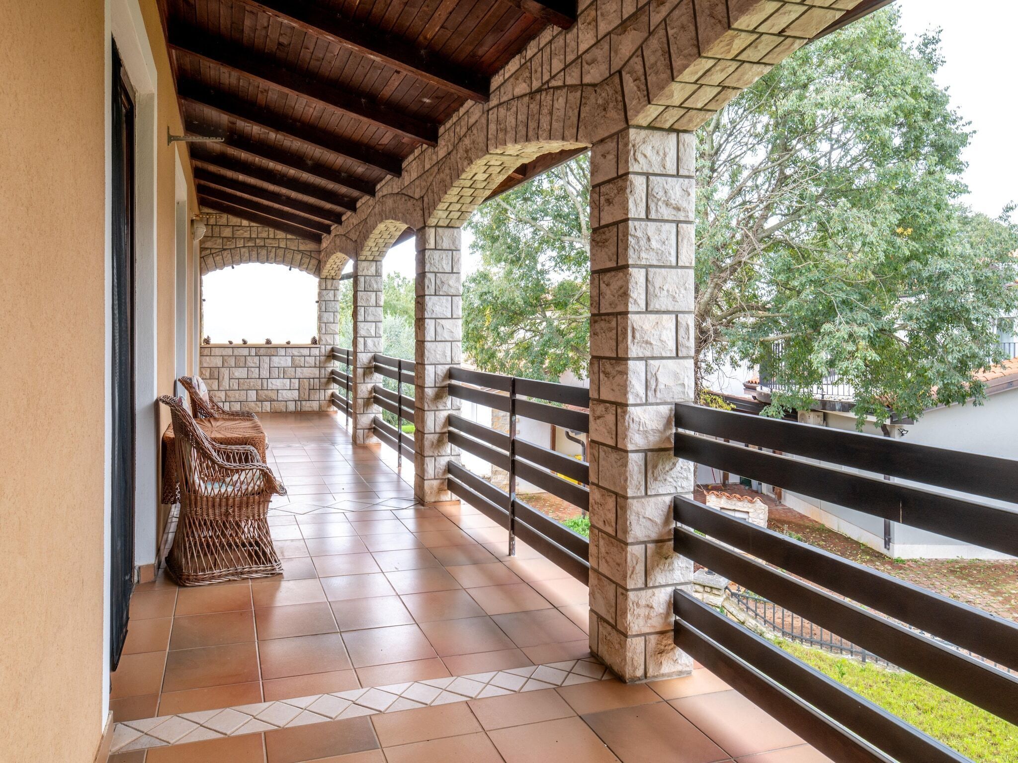 A covered outdoor area with stone pillars, a wooden ceiling, and a tiled floor.