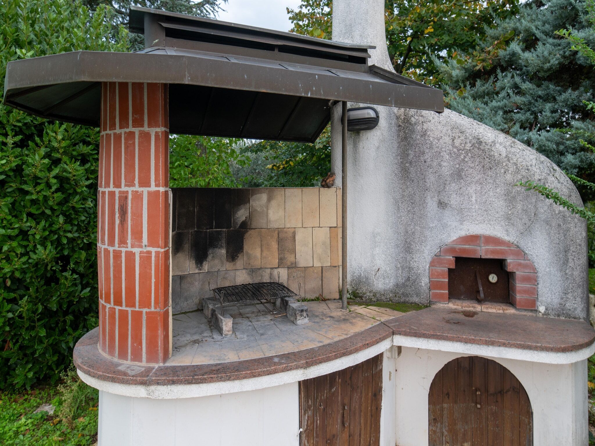 Une cuisine extérieure en briques, dotée d’une cheminée, d’un barbecue et d’un four à pizza.