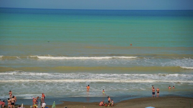 Una spiaggia con persone che si divertono in acqua e sulla sabbia.