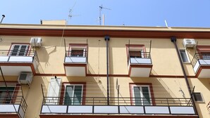 Un edifici de diverses plantes amb balcons, aparells d'aire condicionat i un cel blau clar.