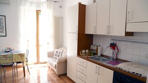 Una cuina compacta amb armaris blancs, forn integrat i menjador amb taula i cadires.
