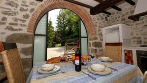 Un comedor con pared de piedra, ventana arqueada y una mesa para dos, con copas de vino, platos y una botella.
