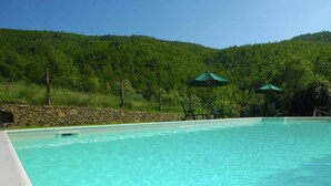Una piscina cristalina con una pared de piedra y sombrillas verdes.