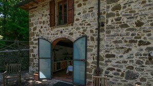 Un edificio de piedra con un arco de entrada que da a una zona de cocina. Hay una mesa redonda con una bandeja de comida y copas de vino tinto.