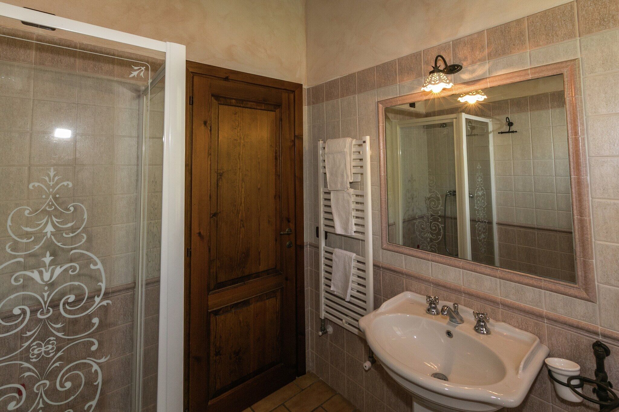 Une salle de bain avec une porte en bois, un lavabo blanc et un miroir doté d’un luminaire.