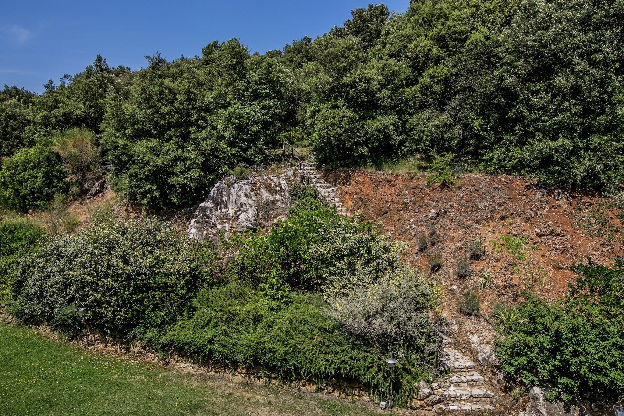 Een natuurlandschap met een stenen trap die omhoog voert over een rotsachtige heuvel, omgeven door weelderige groene begroeiing.