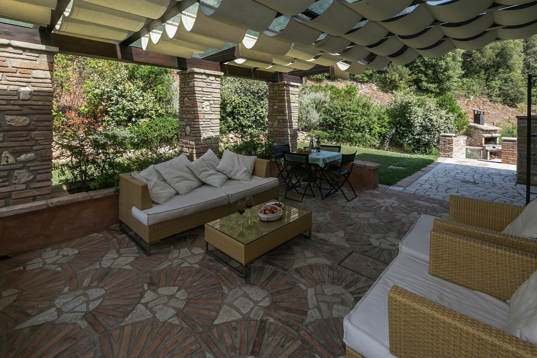 An outdoor patio with a stone floor, a sofa, a dining table, and a covered area with a pergola.