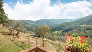 Una vista panorámica desde un balcón con barandilla de madera que da a un valle y colinas al fondo.