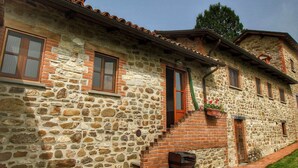 Un edificio de piedra con puerta y ventanas de madera, una escalera de ladrillo y un pequeño jardín.