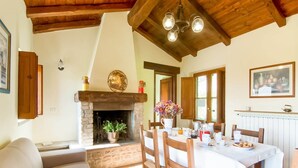 Una sala de estar acogedora con chimenea, una mesa de comedor preparada para cuatro personas y un sofá confortable.