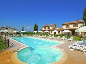 A swimming pool with lounge chairs and umbrellas, surrounded by buildings with tiled roofs and a clear blue sky.