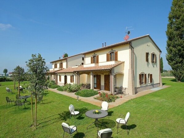 A two-story house with a patio area, outdoor seating, and a garden.