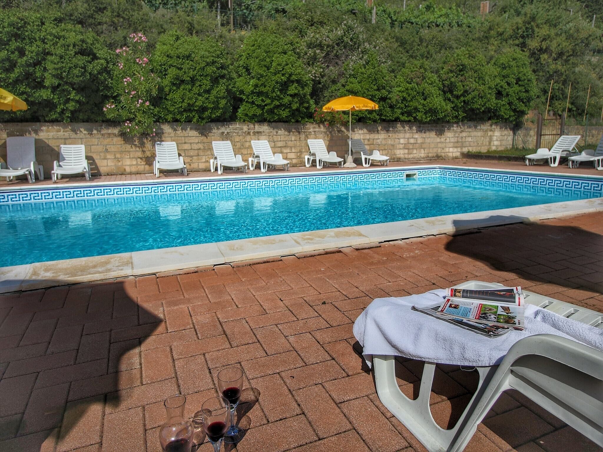 Une piscine bordée de chaises longues blanches, avec une table où sont disposées des boissons et des menus.