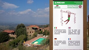 Placa para um parque de atividades físicas com instruções em vários idiomas, com vista para uma área de piscina e casas ao fundo.