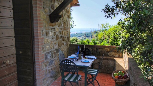 Um edifício de pedra com uma mesa posta para dois, uma cesta de frutas e vista para o campo.