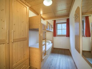 A room with wooden bunk beds, a wardrobe, and a window with curtains.