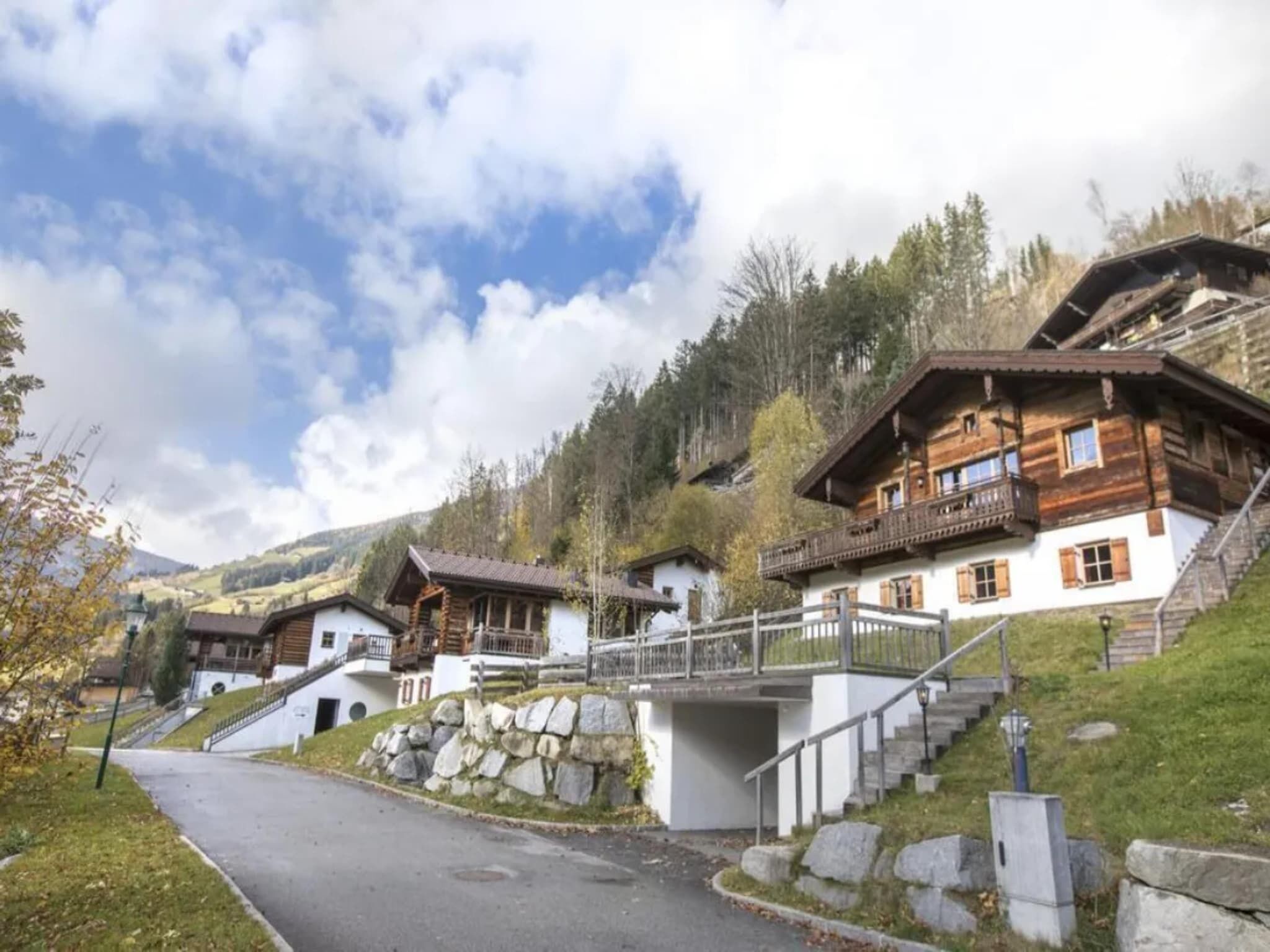 A cluster of traditional wooden houses with stone foundations, set against a backdrop of hills and a clear sky.