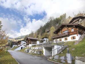 A cluster of traditional wooden houses with stone foundations, set against a backdrop of hills and a clear sky.