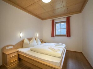 A bedroom with a wooden ceiling, a bed with white bedding, a nightstand, and a window with red curtains. - Holiday Home near Zillertal Arena (Wald-Königsleiten)