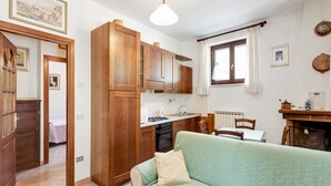 A compact kitchen with wooden cabinets, a stove, and a sink. There is a dining table with chairs and a green sofa in the living area.