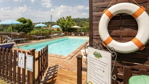 A pool area with a wooden fence, lounge chairs, and umbrellas.
