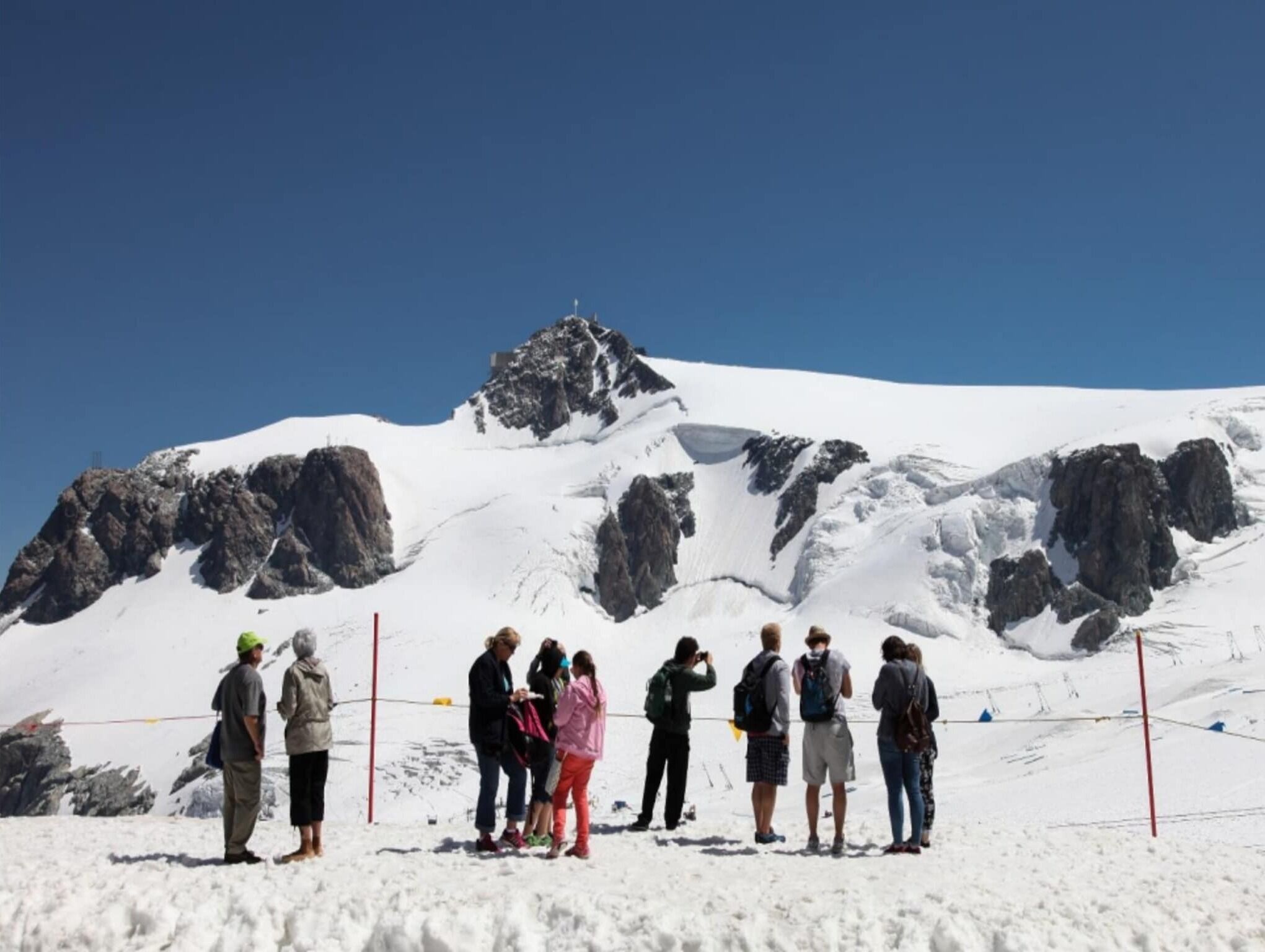 Eine Gruppe von Menschen steht auf einem verschneiten Berg, im Hintergrund ein felsiger Gipfel.