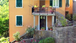 A two-story house with a balcony, a stone staircase, and potted plants.