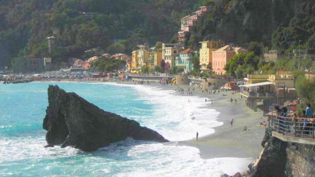 A coastal town with colorful buildings, a rocky outcrop in the water, and a beach with people.