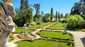 Un jardín formal con céspedes cuidados, senderos geométricos y estatuas clásicas.