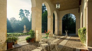 Un patio al aire libre con una mesa y sillas, rodeado de columnas de piedra y plantas en macetas.